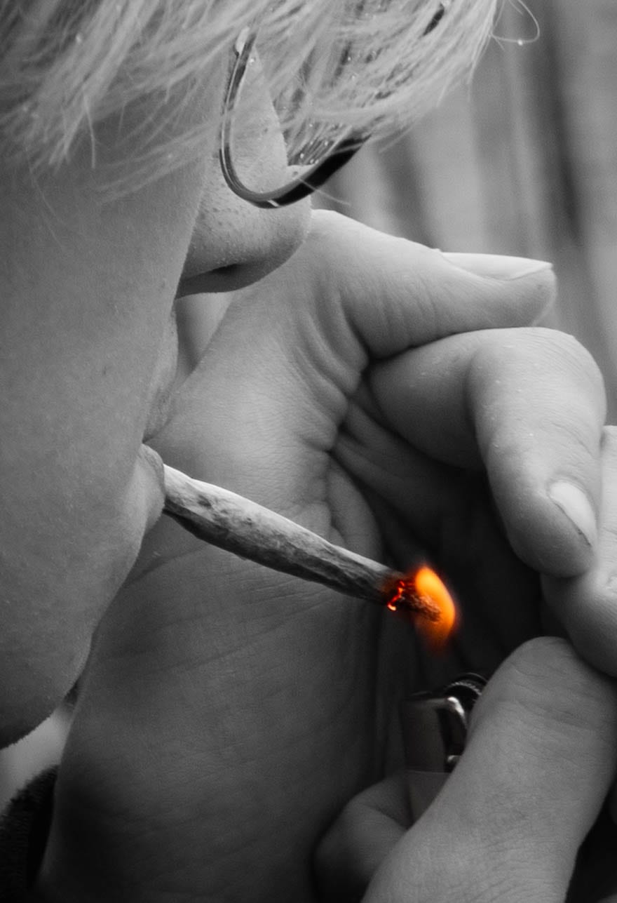 Black and white close-up of a cigarette being lit, with only the orange flame in color